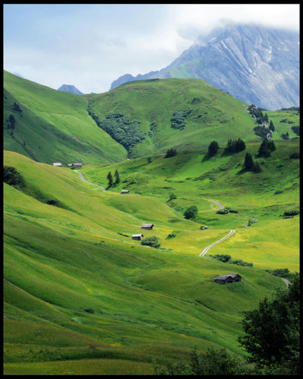 Leinwandbild von einer grünen Berglandschaft mit einzelnen Bäumen und Holzhütten.