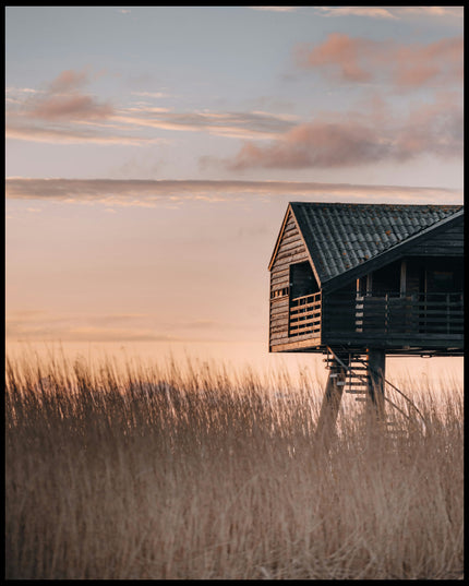 Ein Poster von einer Hütte am Strand in den Dünen bei Sonnenuntergang.