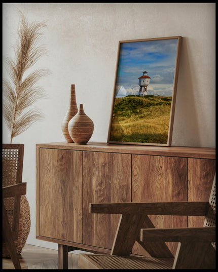 Ein gerahmtes Poster von einem weißen Wasserturm auf der Insel Langeoog, auf einer Holzkommode an die Wand angelehnt