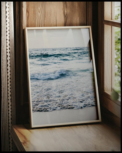 Ein gerahmtes Poster von schaumigen Wellen am Strand, vor einem Fenster an die Wand angelehnt