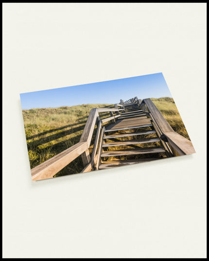 Eine Postkarte von einer Holztreppe die über Dünen am Strand führt.